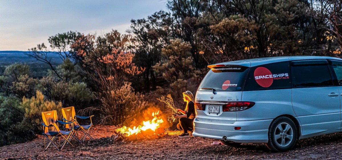 Camper creating a small campfire in an area where it's allowed: not too close to the campervan or the bushes, with plenty of sand around