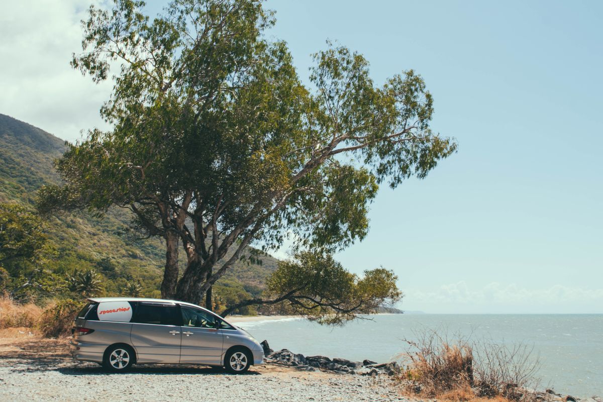 Campervan parked under a tree near the ocean so its Space Travellers can enjoy the scenery